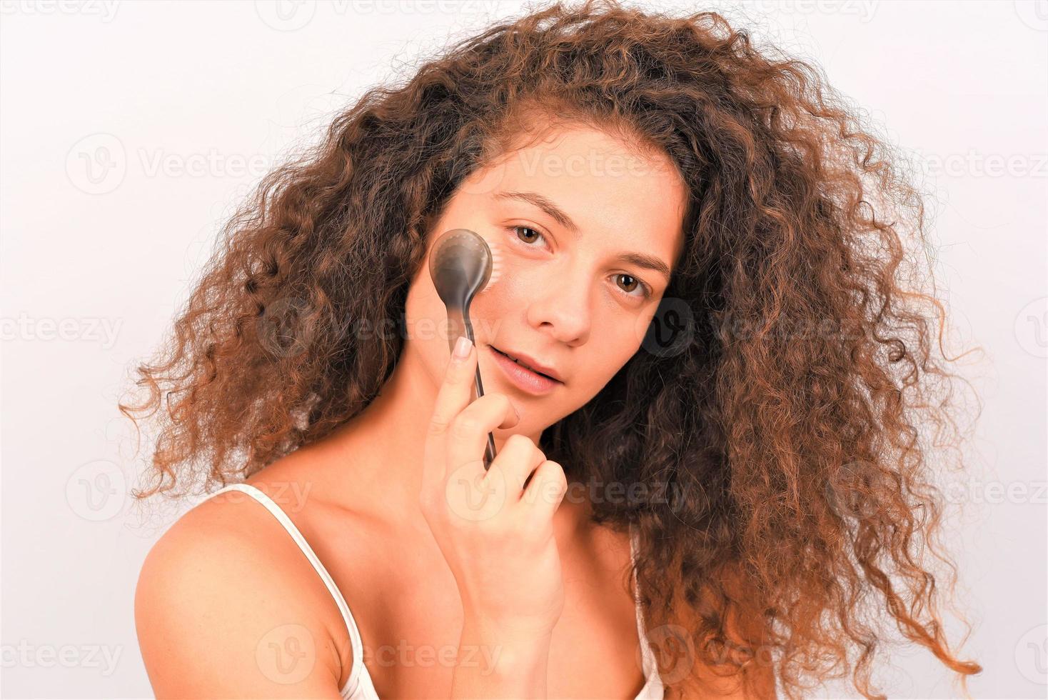 Beautiful young woman is washing her face with face brush photo