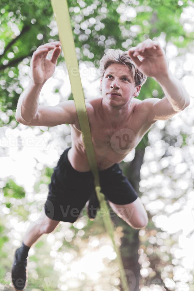 Young man balancing and jumping on slackline. Man walking, jumping and balancing on rope in park. photo