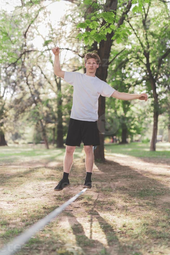 Young man balancing and jumping on slackline. Man walking, jumping and balancing on rope in park. photo