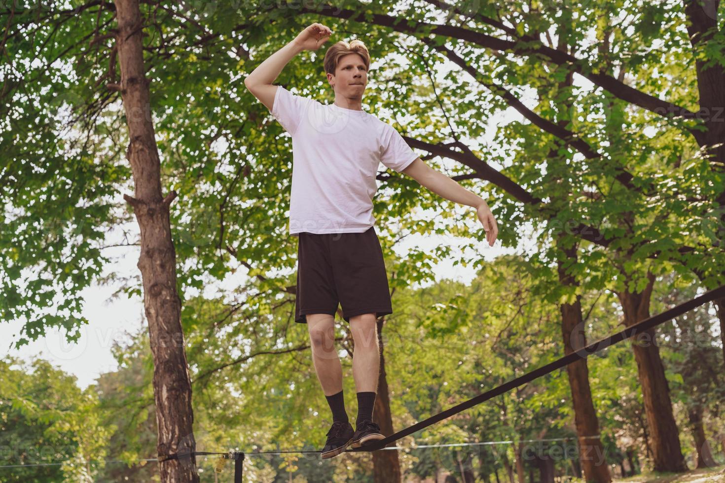 Young man balancing and jumping on slackline. Man walking, jumping and balancing on rope in park. photo