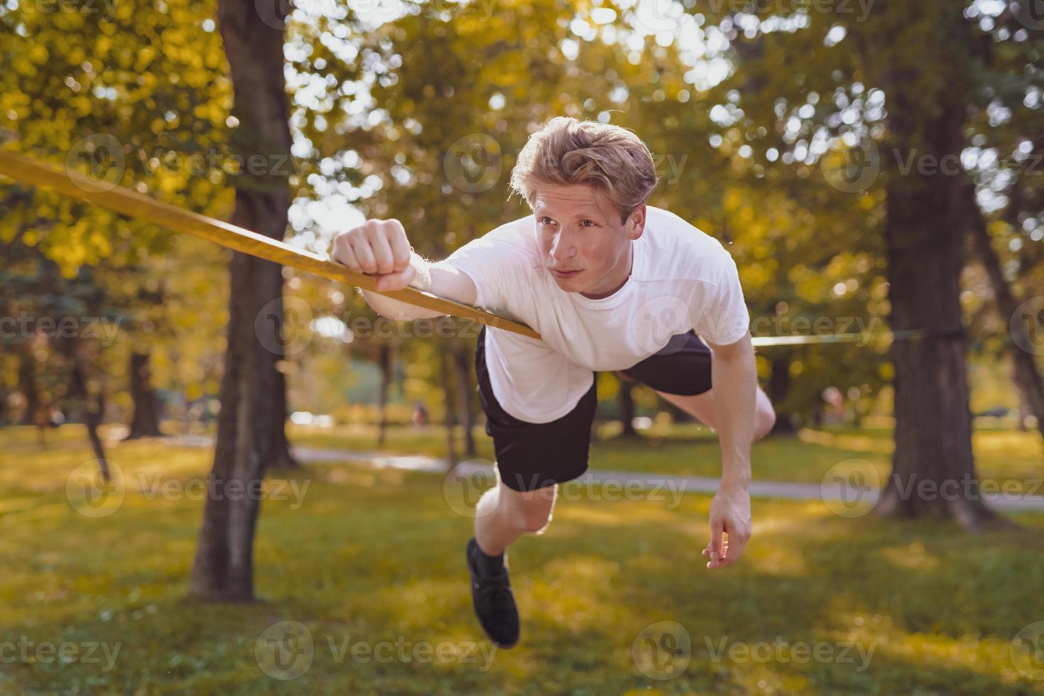 joven balanceándose y saltando en slackline. hombre caminando, saltando y balanceándose en la cuerda en el parque. foto