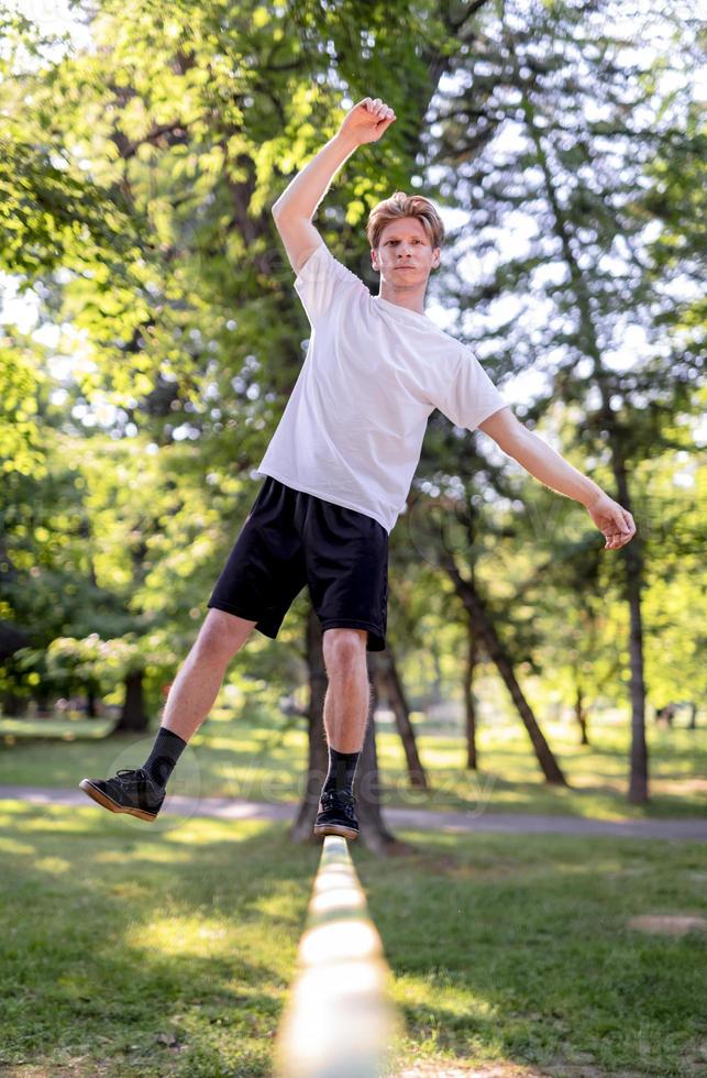 Young man balancing and jumping on slackline. Man walking, jumping and balancing on rope in park. photo