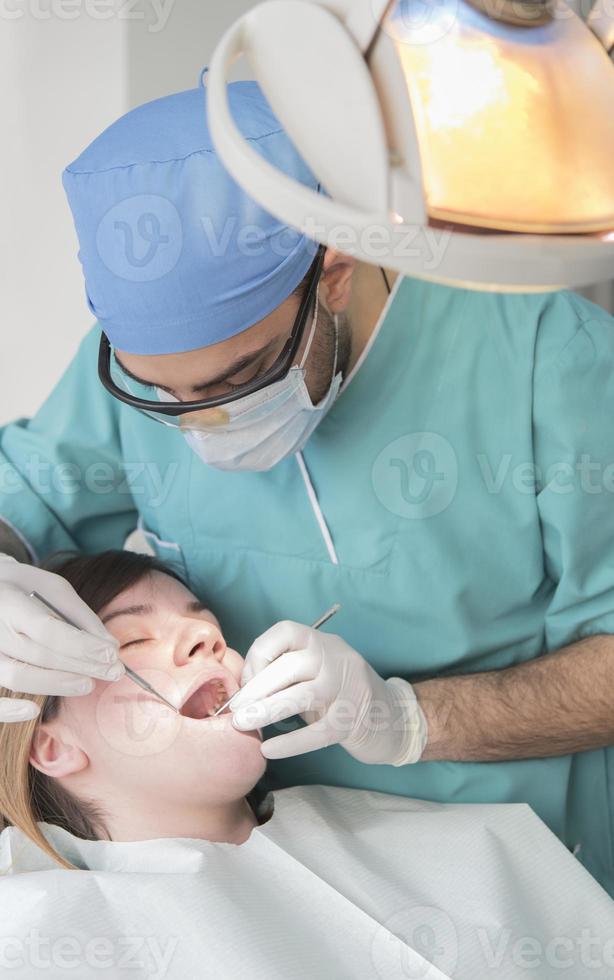 Young male dentist curing patient's teeth filling cavity. Dentist working with professional equipment in clinic. photo