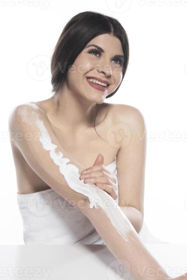 Beautiful skinned woman applying body lotion on white background photo