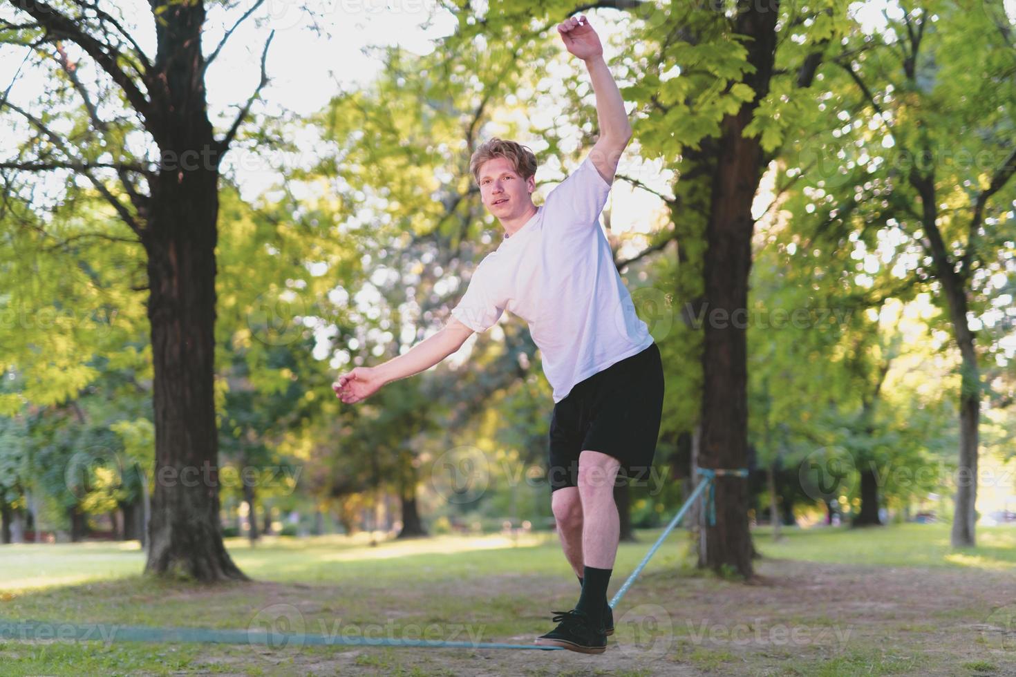 Young man balancing and jumping on slackline. Man walking, jumping and balancing on rope in park. photo