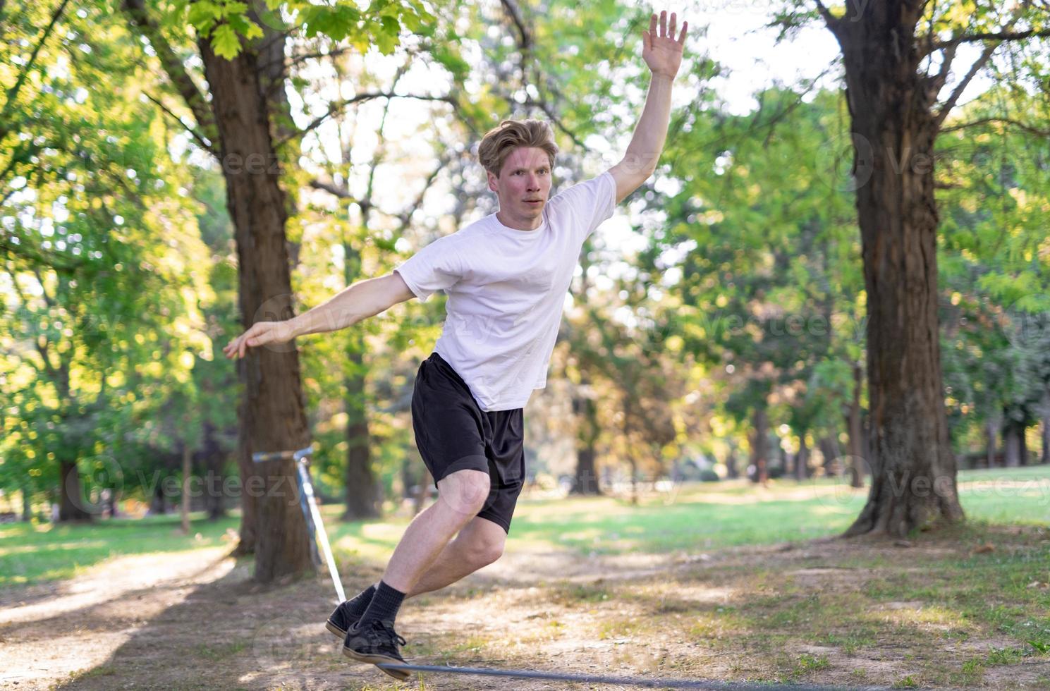 Young man balancing and jumping on slackline. Man walking, jumping and balancing on rope in park. photo