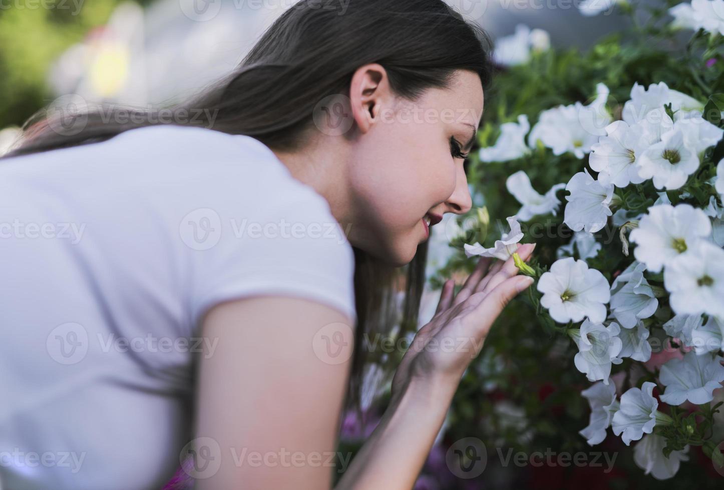 Young woman at a nursery holding flower plant in her hands as she kneels in the walkway between plants. photo