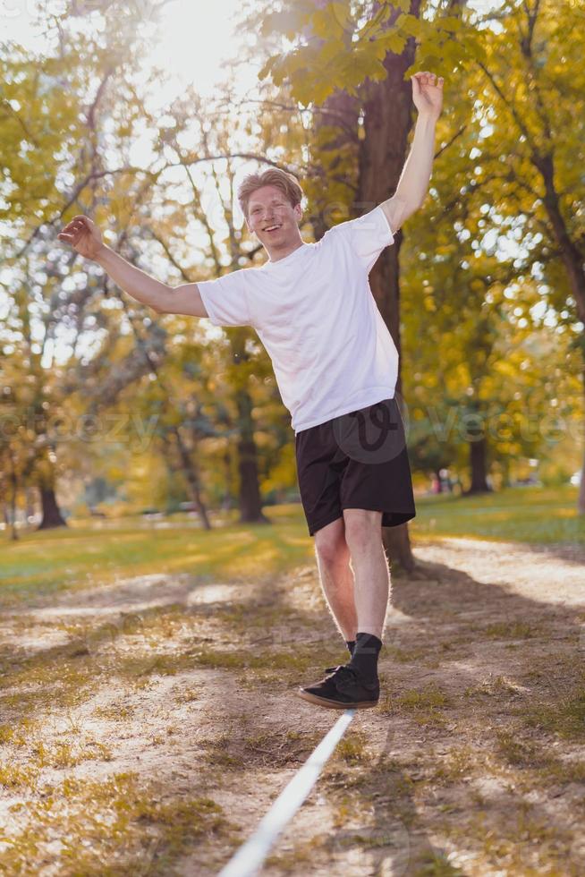 Young man balancing and jumping on slackline. Man walking, jumping and balancing on rope in park. photo