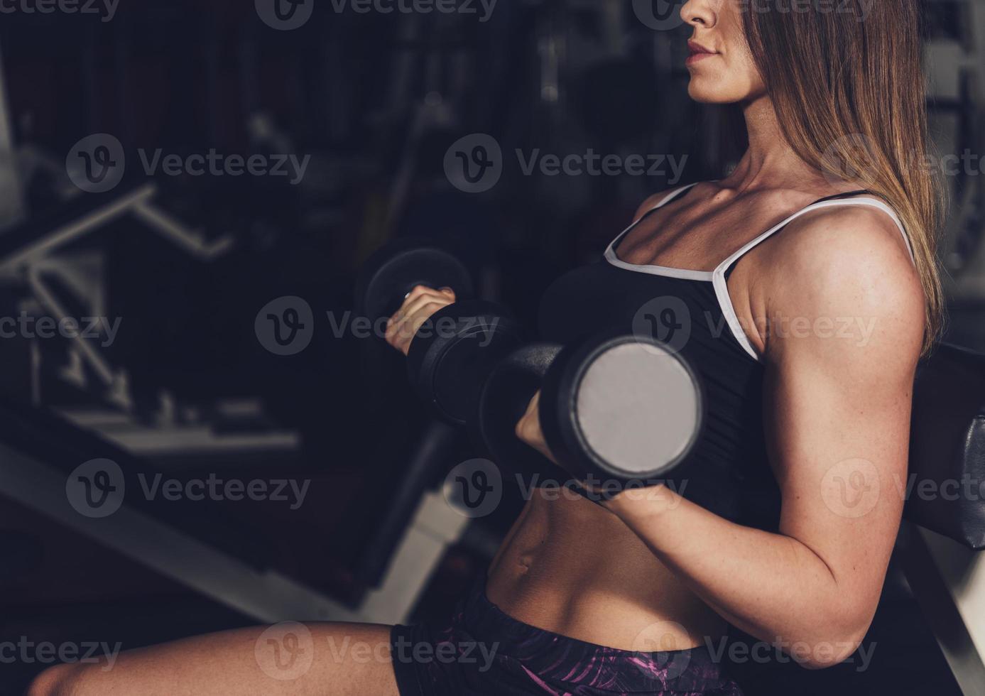 mujer culturista con cuerpo bronceado haciendo ejercicio en el gimnasio levantando pesas foto
