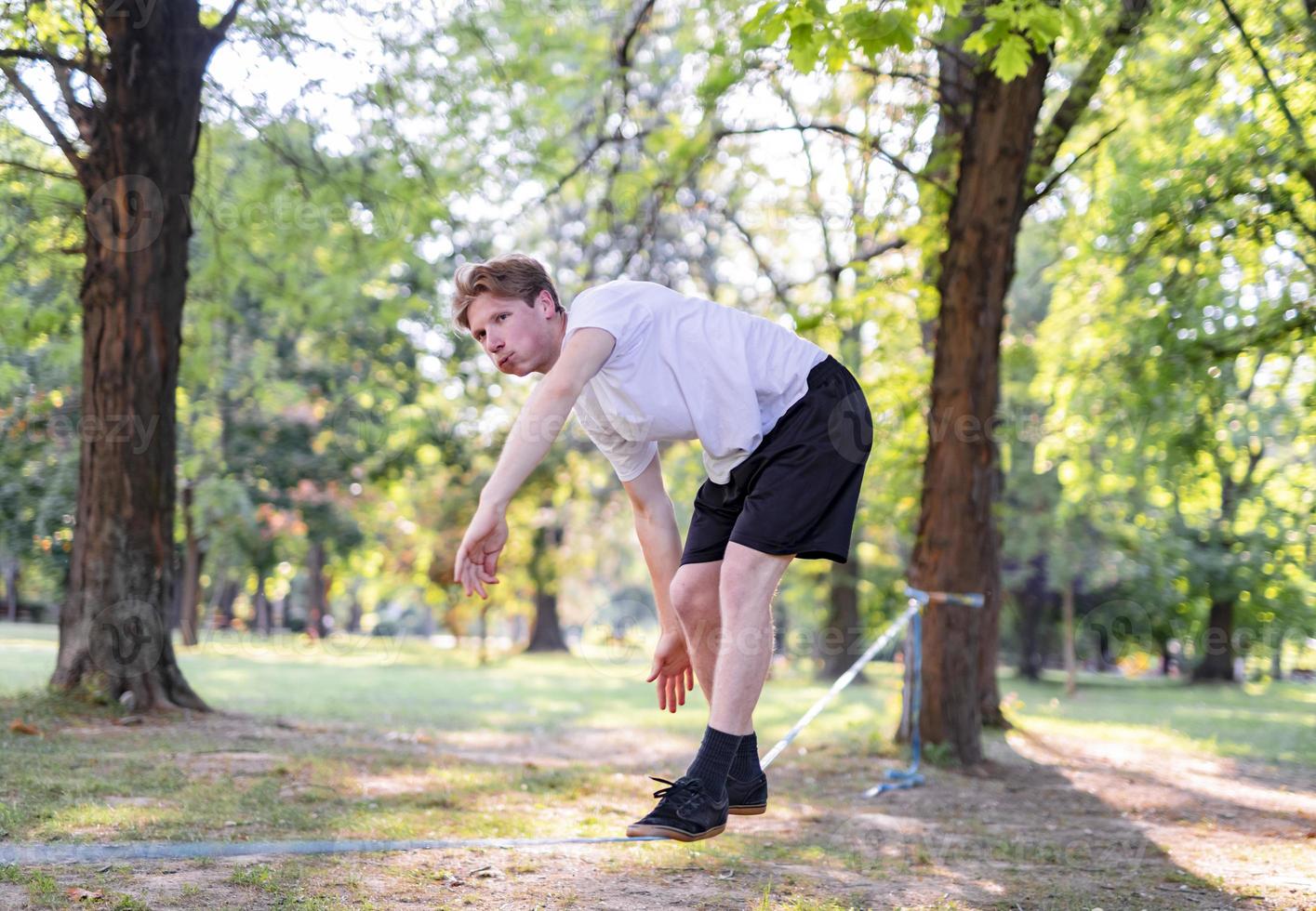 joven balanceándose y saltando en slackline. hombre caminando, saltando y balanceándose en la cuerda en el parque. foto