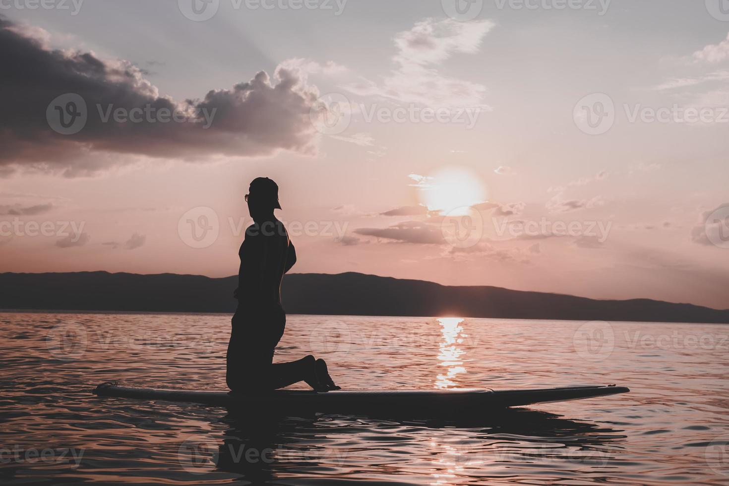 Sporty young man on SUP paddle board going to the sea at sunset. photo