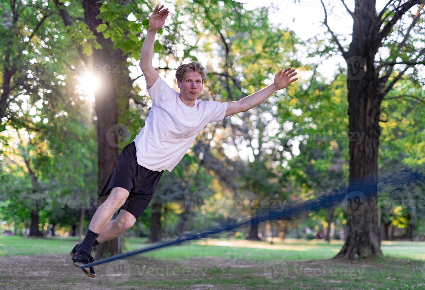 joven balanceándose y saltando en slackline. hombre caminando, saltando y balanceándose en la cuerda en el parque. foto