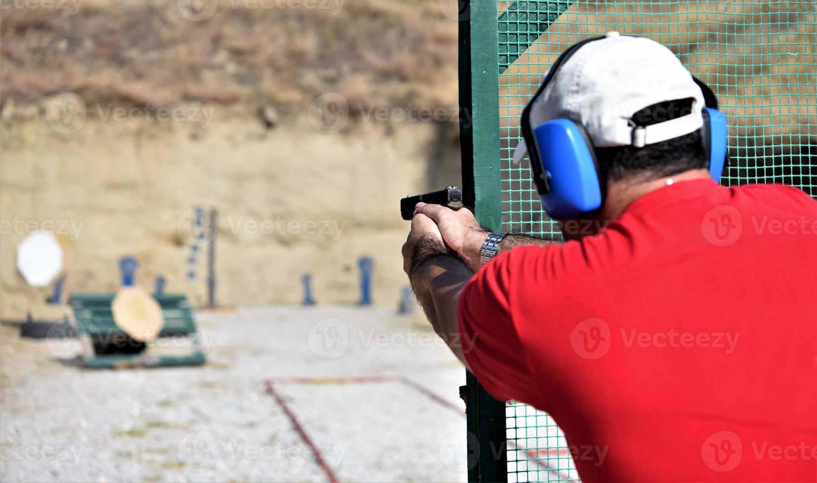 vista trasera de un hombre disparando su arma en un rancho de práctica. foto