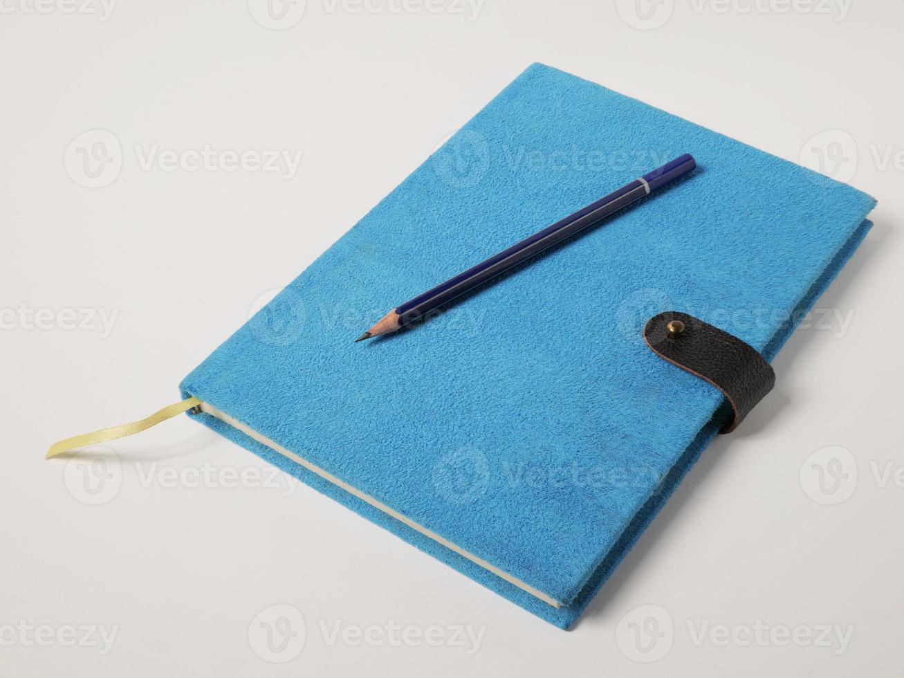 The notebook cover is a blue velvet skin with a flap locking flap. There is a wooden pencil on top. White background. photo