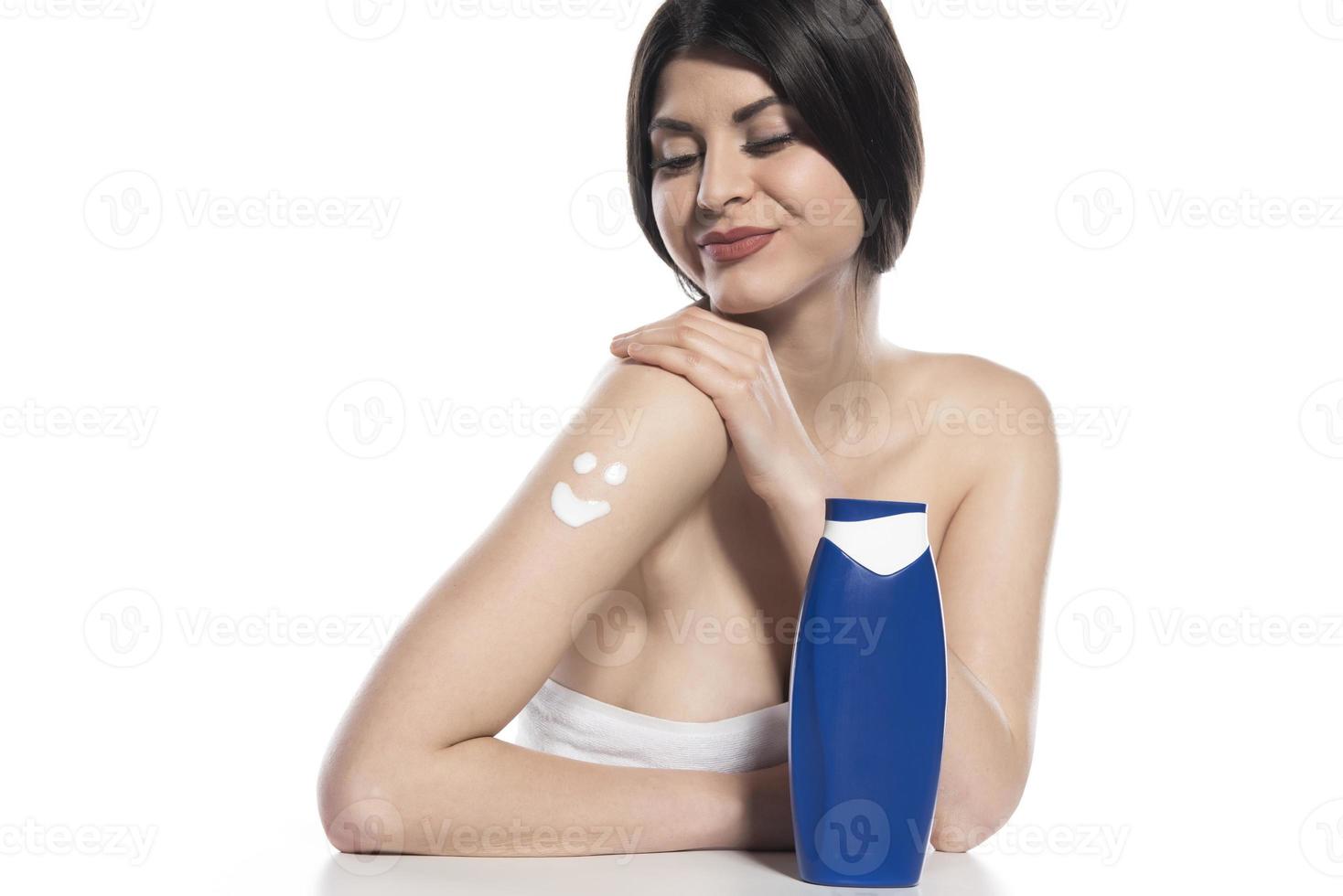 Beautiful skinned woman applying body lotion on white background photo