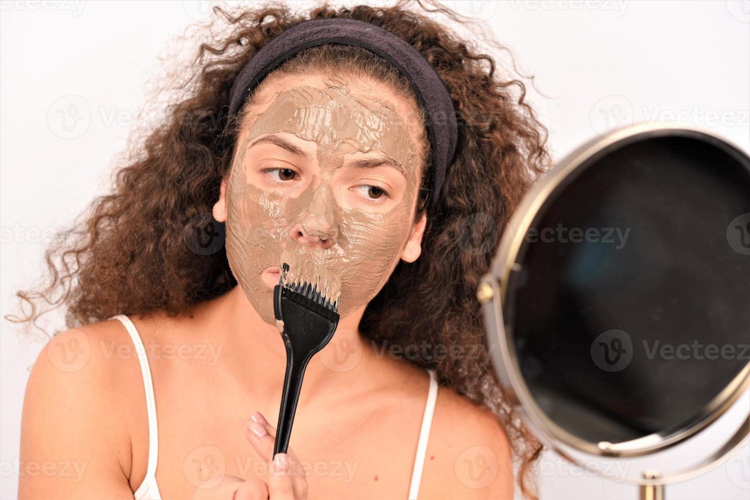 Beauty procedures skin care concept. Young woman applying facial gray mud clay mask to her face photo