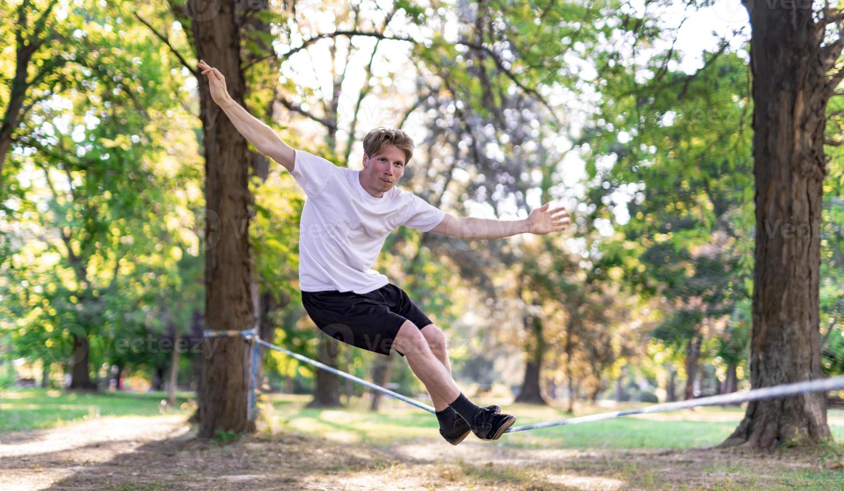 Young man balancing and jumping on slackline. Man walking, jumping and balancing on rope in park. photo