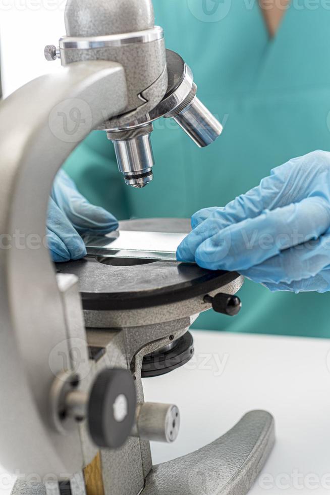 científico con guantes médicos azules y muestras uniformes de aprendizaje covid-19 con microscopio en laboratorio. foto