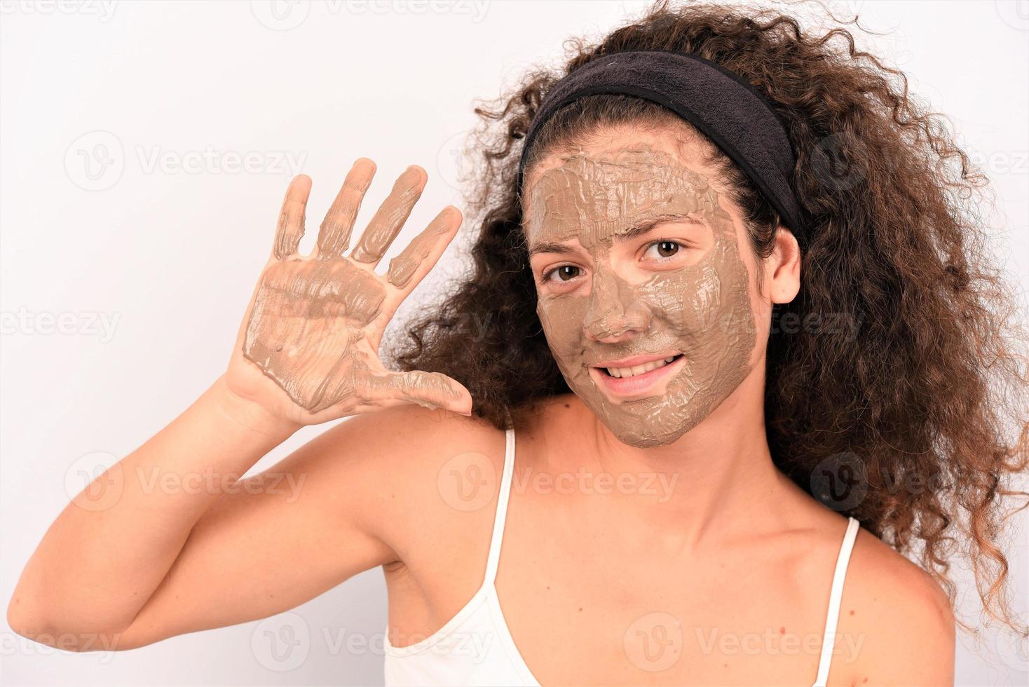 Beauty procedures skin care concept. Young woman applying facial gray mud clay mask to her face photo