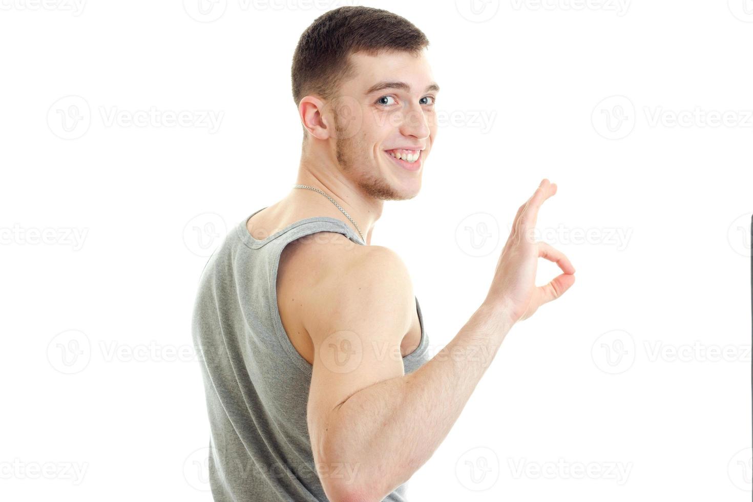 handsome young sporty guy stands sideways looks forward smiles and hand gesture Okey photo