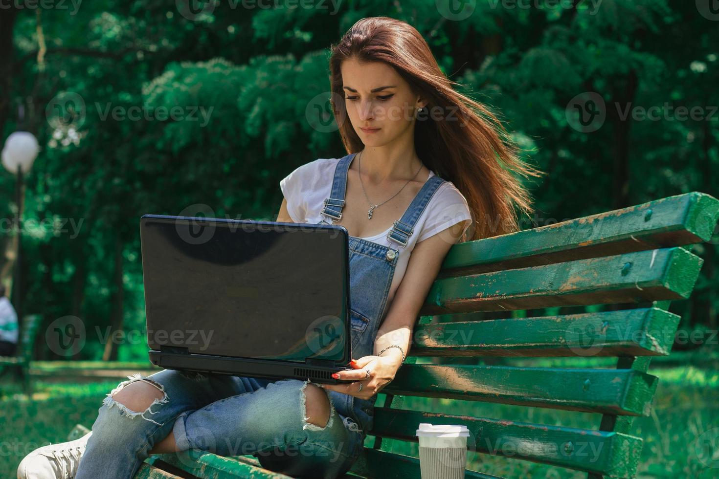 beautiful girl with long hair sitting in a Green Park and looking at laptop photo