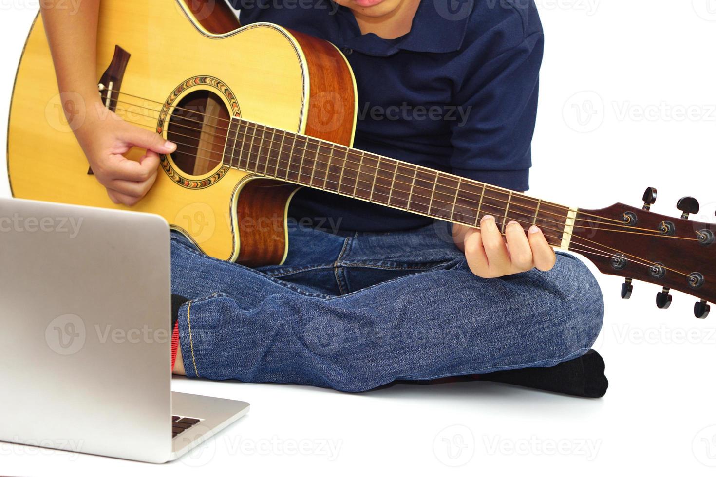 Focus on the hands of the child or teenager playing acoustic guitar and a laptop in the foreground on white background. Learning and relax concept. photo