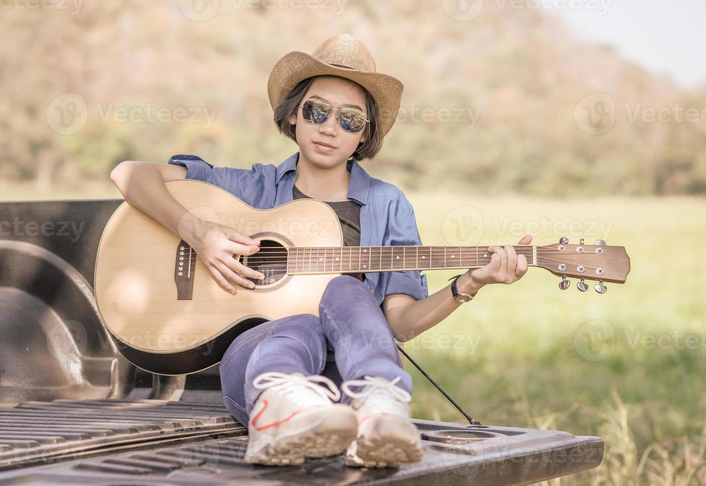 Woman wear hat and playing guitar on pickup truck photo