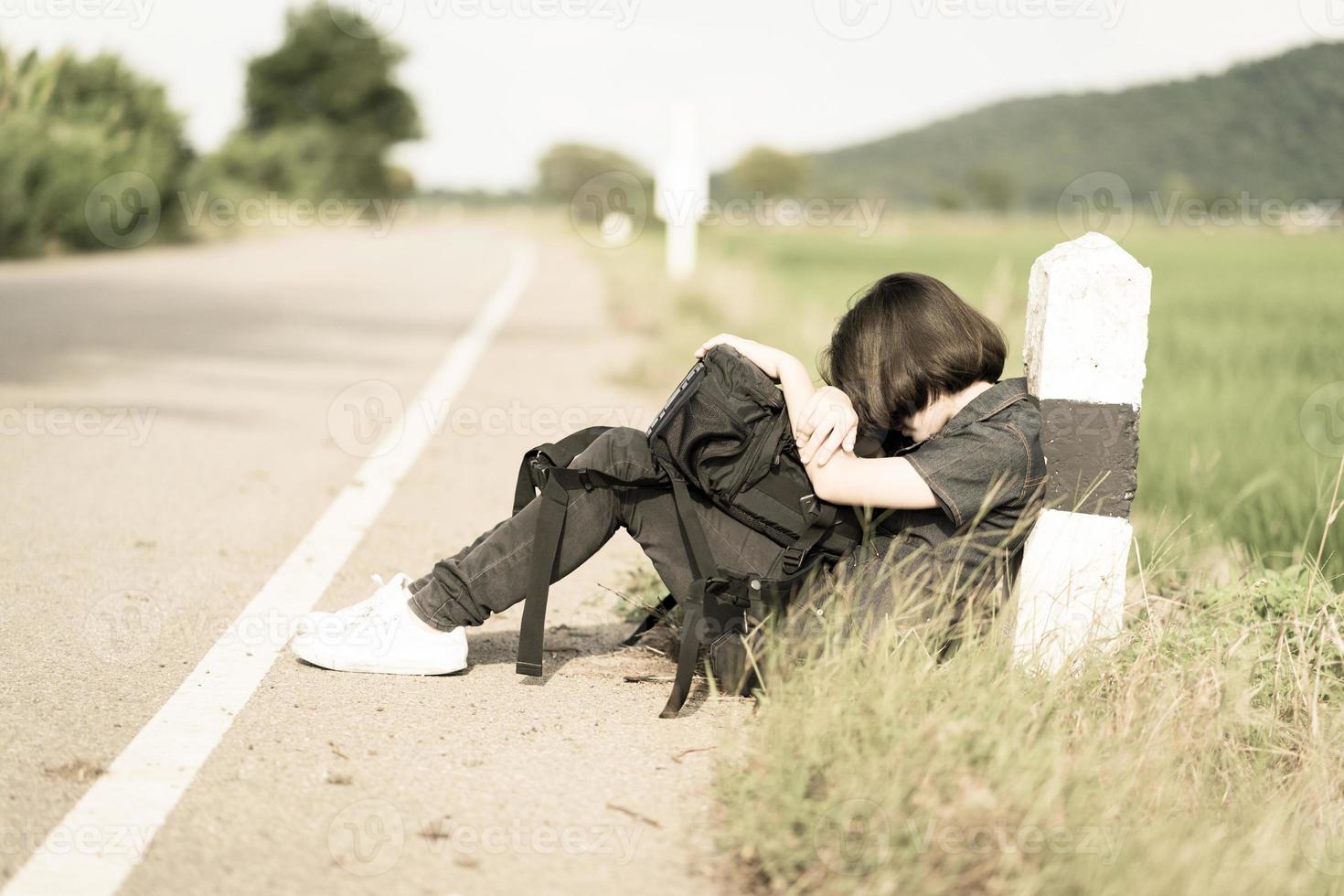 Woman sit with backpack hitchhiking along a road photo