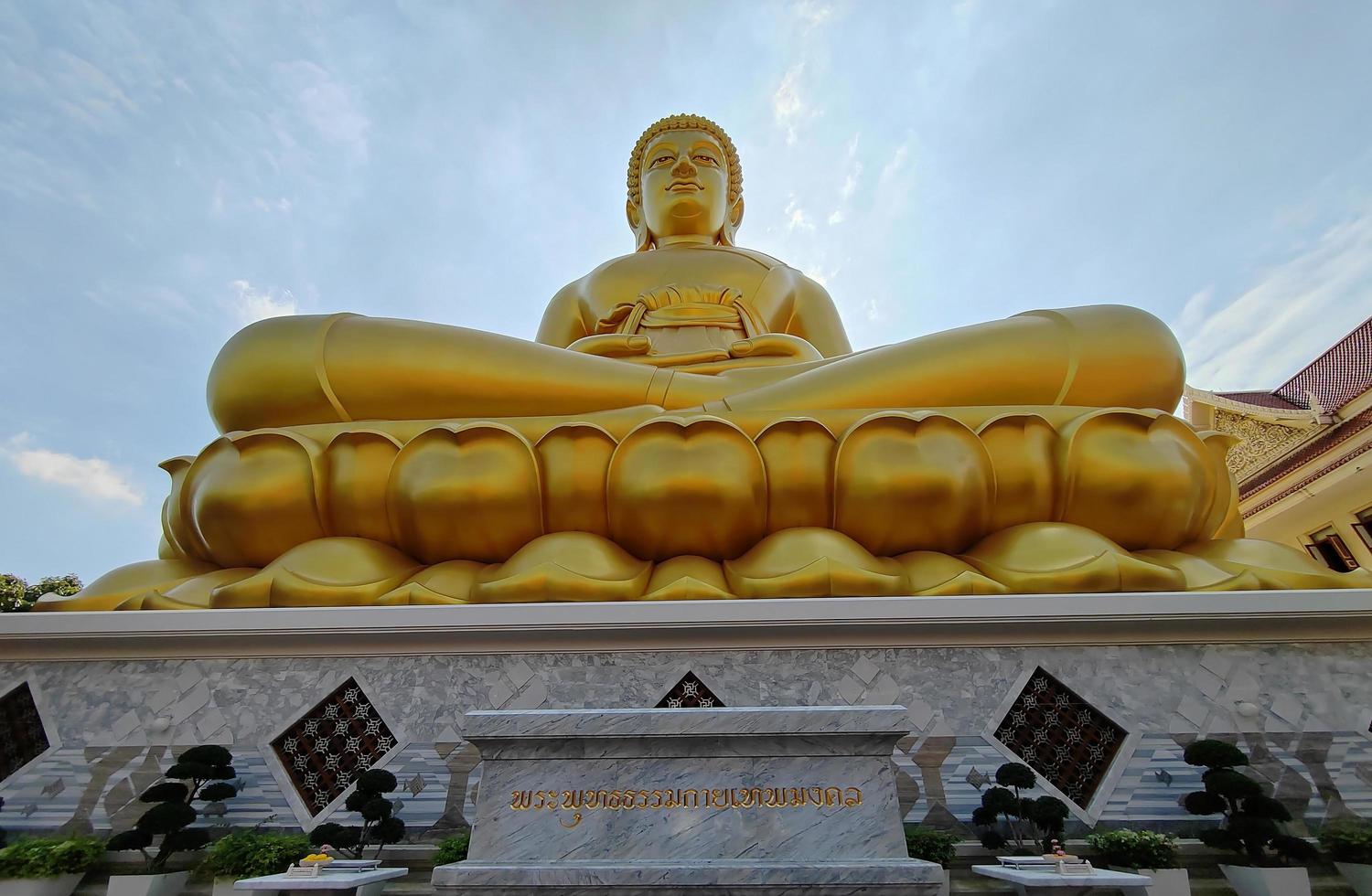 vista frontal estatua dorada del gran buda phra buddha dhammakaya thep mongkol, traducir el idioma en el templo wat pak nam phasi charoen. luz del sol cielo y fondo de nubes foto