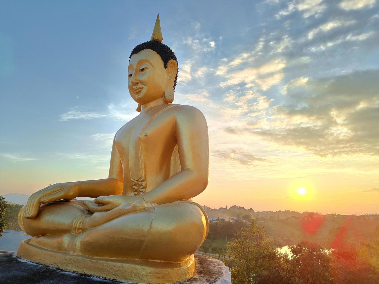 Vista lateral de la estatua dorada de Buda contra el cielo del atardecer en el templo de Tailandia foto