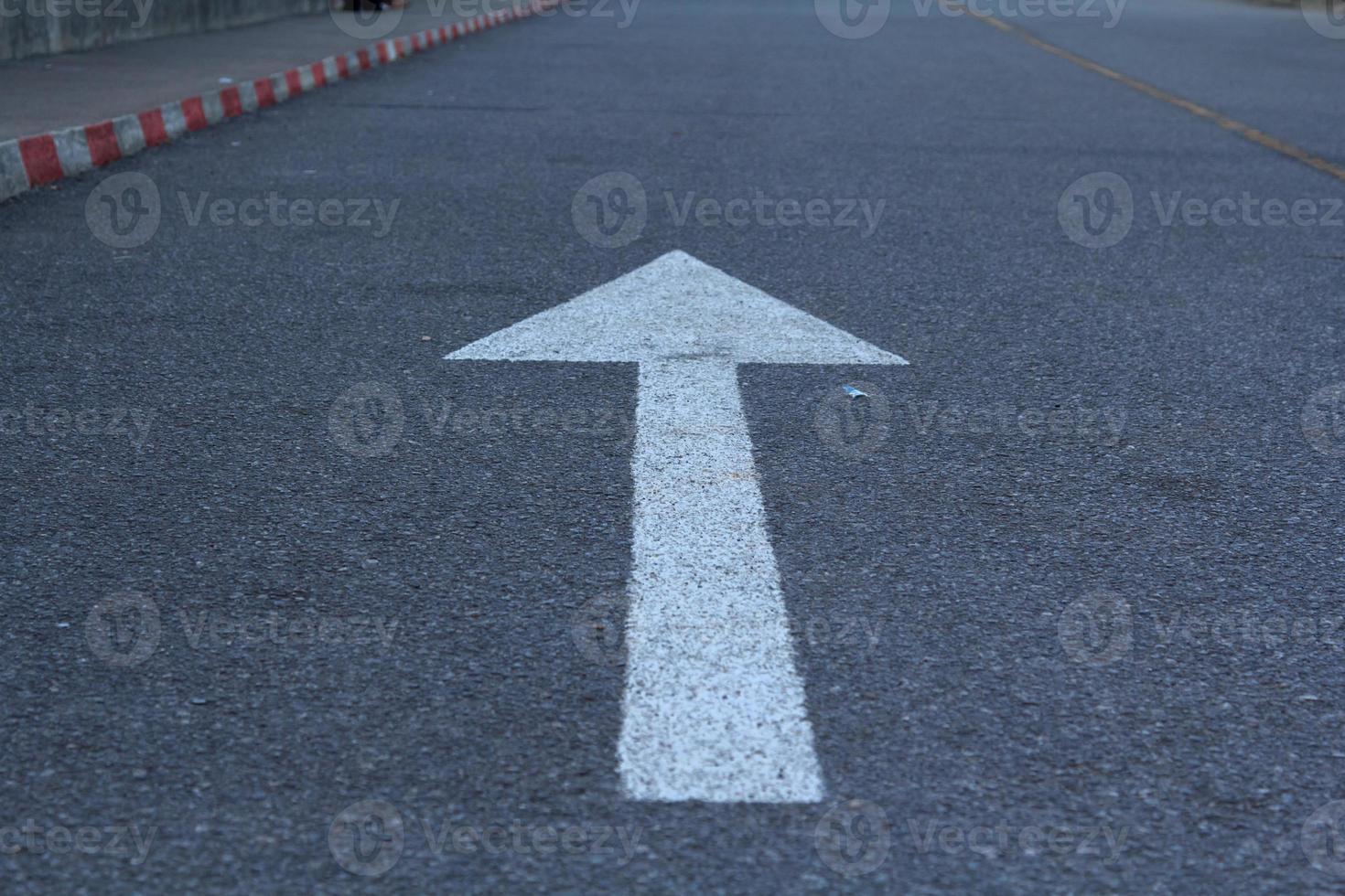 white arrow traffic sign on black asphalt on the road is a straight forward symbol used throughout the world. photo