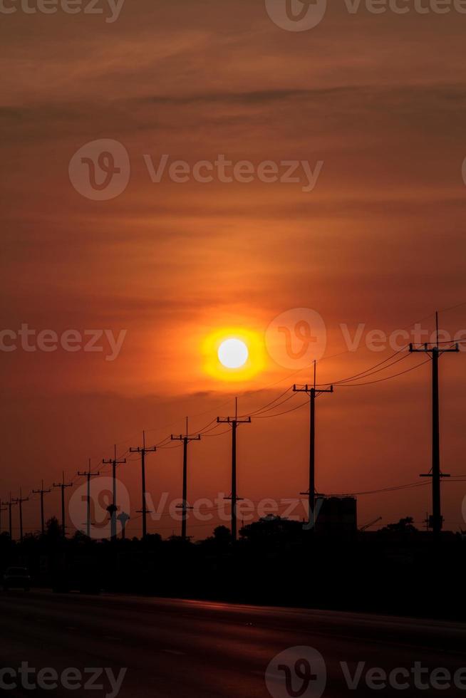 atmosphere in the evening-high voltage pole beside highway and orange sky The big sun that was setting was beautiful as I was on my way home, it was a beautiful romantic atmosphere. photo