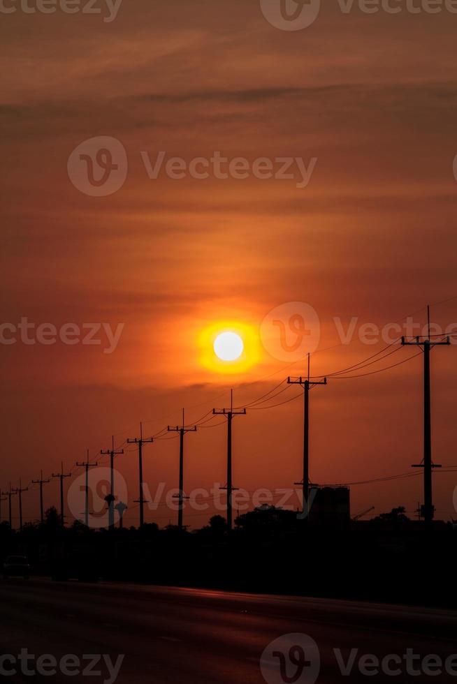 Atmósfera en el poste de alto voltaje de la tarde al lado de la carretera y el cielo anaranjado. El gran sol que se estaba poniendo era hermoso cuando estaba de camino a casa, era una hermosa atmósfera romántica. foto