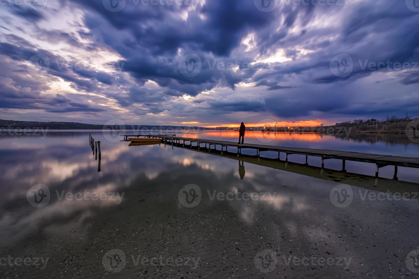 increíble vista tranquila con un bote en el lago y una silueta de una mujer mirando la puesta de sol en el muelle foto