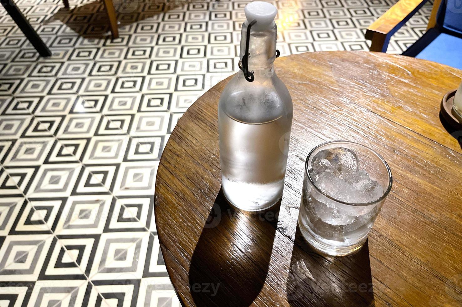 refreshing cold vodka in the bottle with ice rocks in the glass served in the pub photo