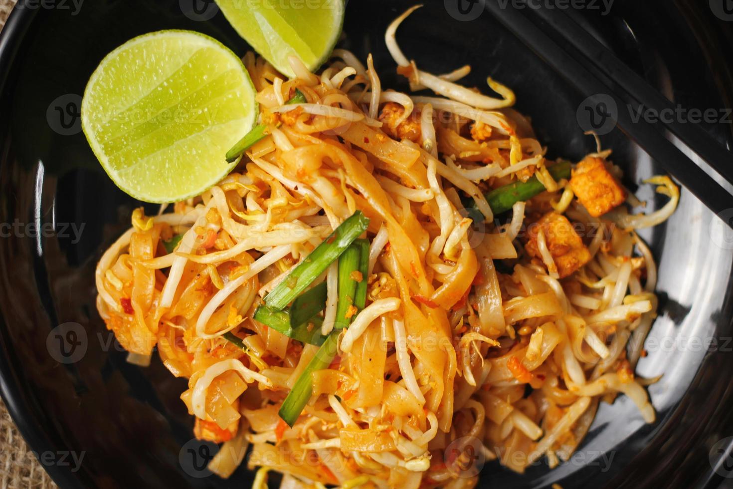 pad thai o pad thai al estilo tailandés servido con lima y condimentos en un plato negro, es una comida que se puede encontrar en la comida callejera de tailandia. foto