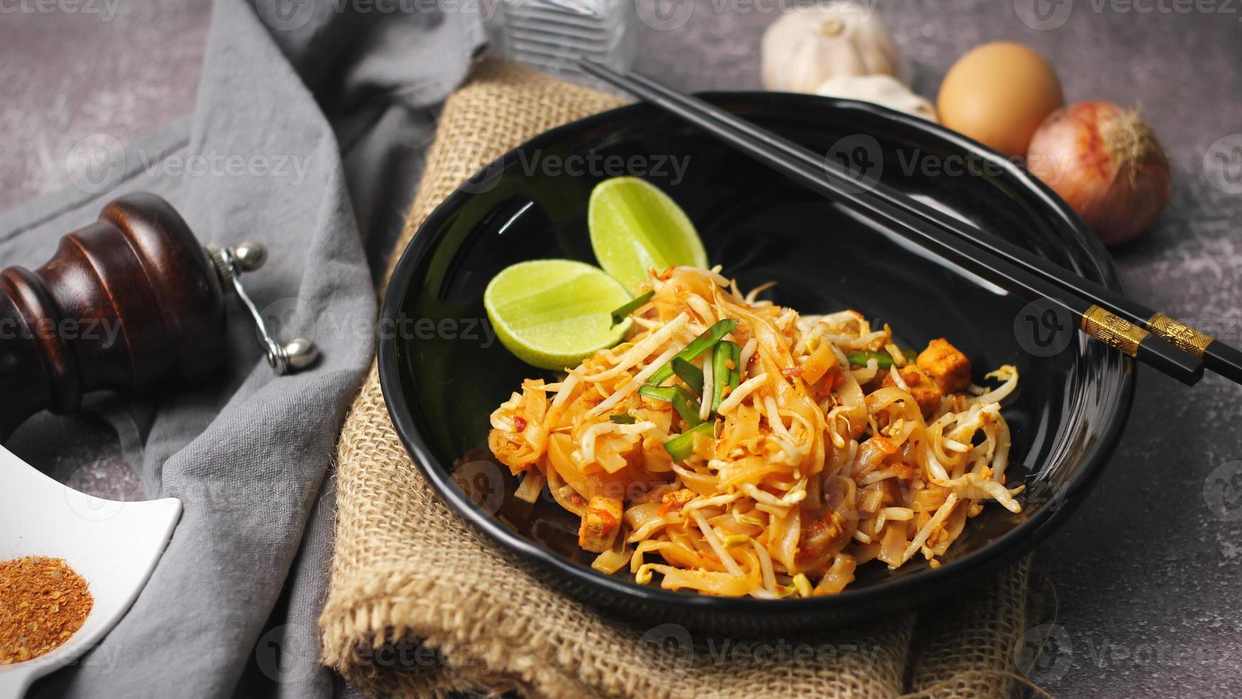 pad thai o pad thai al estilo tailandés servido con lima y condimentos en un plato negro, es una comida que se puede encontrar en la comida callejera de tailandia. foto