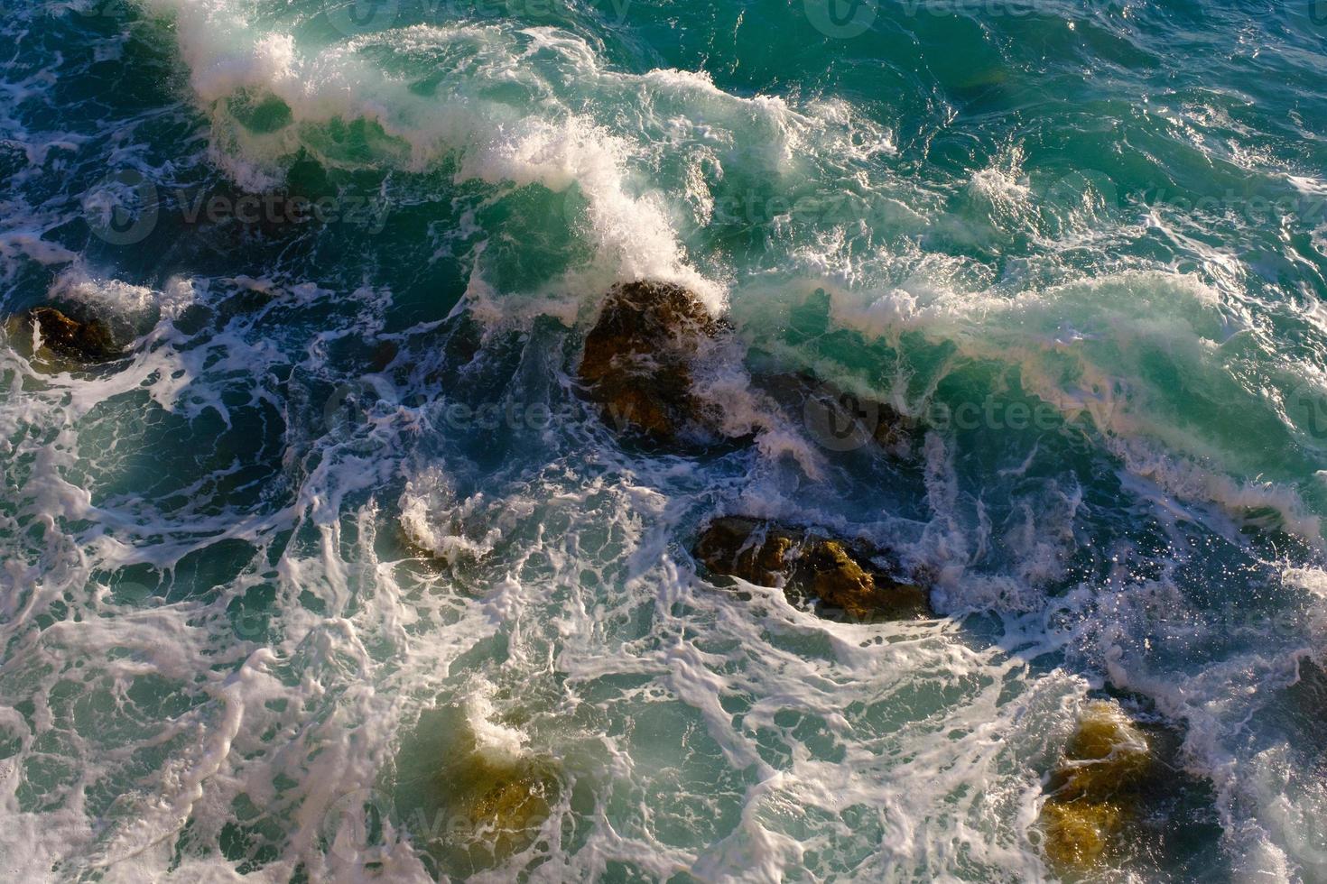 agua de mar rompiendo en rocas, al aire libre, olas y piedras, salpicaduras y espuma, vista superior. foto
