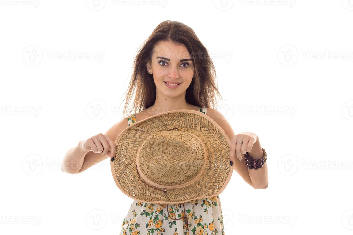young pretty brunette girl in sarafan with floral pattern and straw hat with wide brim smiling on camera isolated on white background photo
