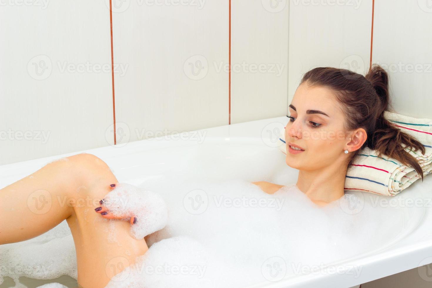 young smiling girl is bathed in a tub with foam photo