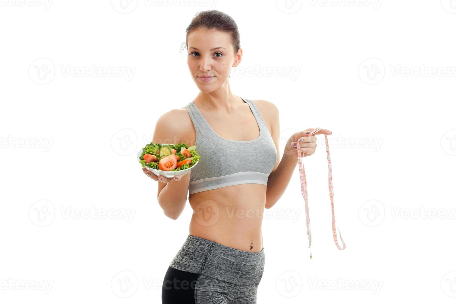 a young athletic girl in top holds a plate of salad and a measuring tape photo