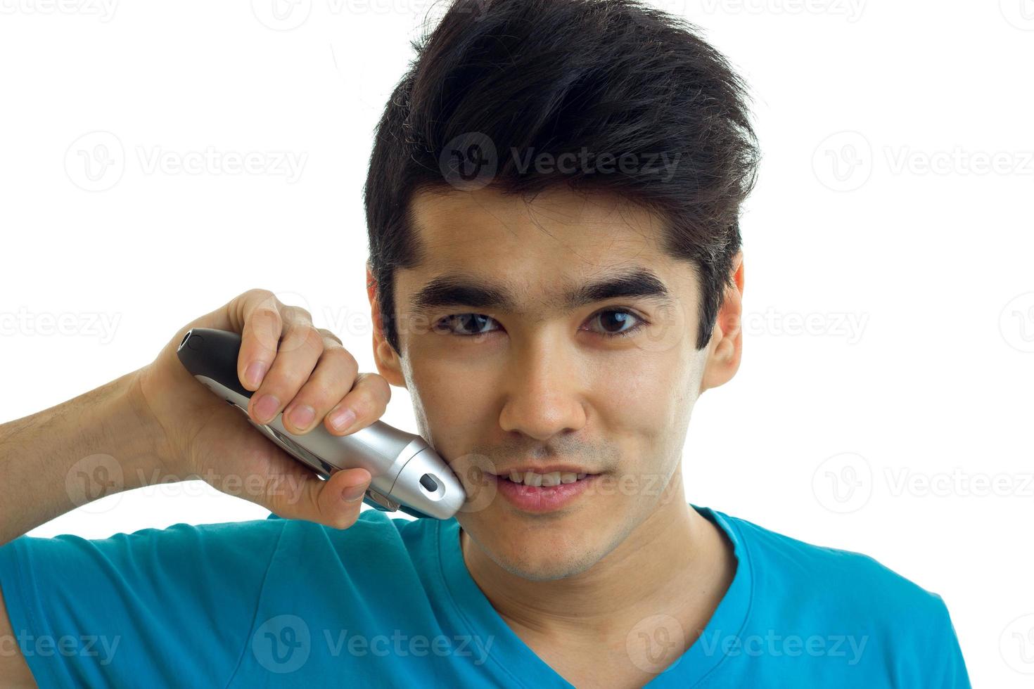 Portrait of a handsome young guy who looks at the camera smiling and shaves the beard trimmer photo