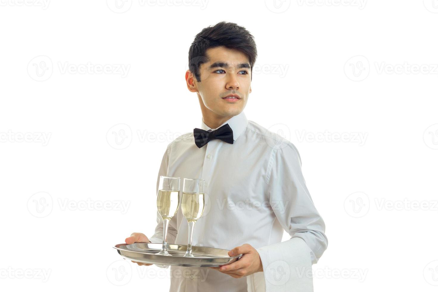 young handsome waiter holding a tray with glasses of champagne and looks toward photo