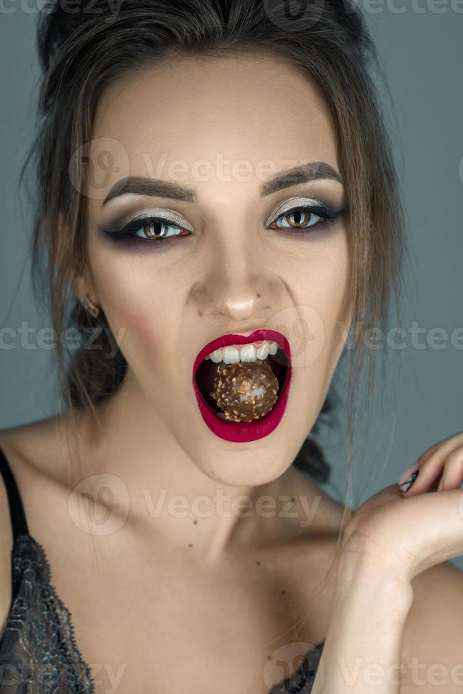 hermosa chica con labios rojos come dulces de chocolate y mira a la cámara foto