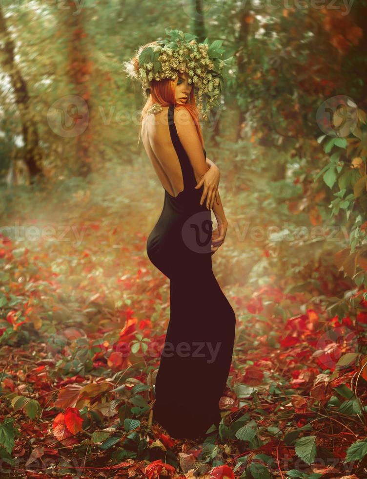 Slim young sexy lady with wreath of hop on red hair in forest photo