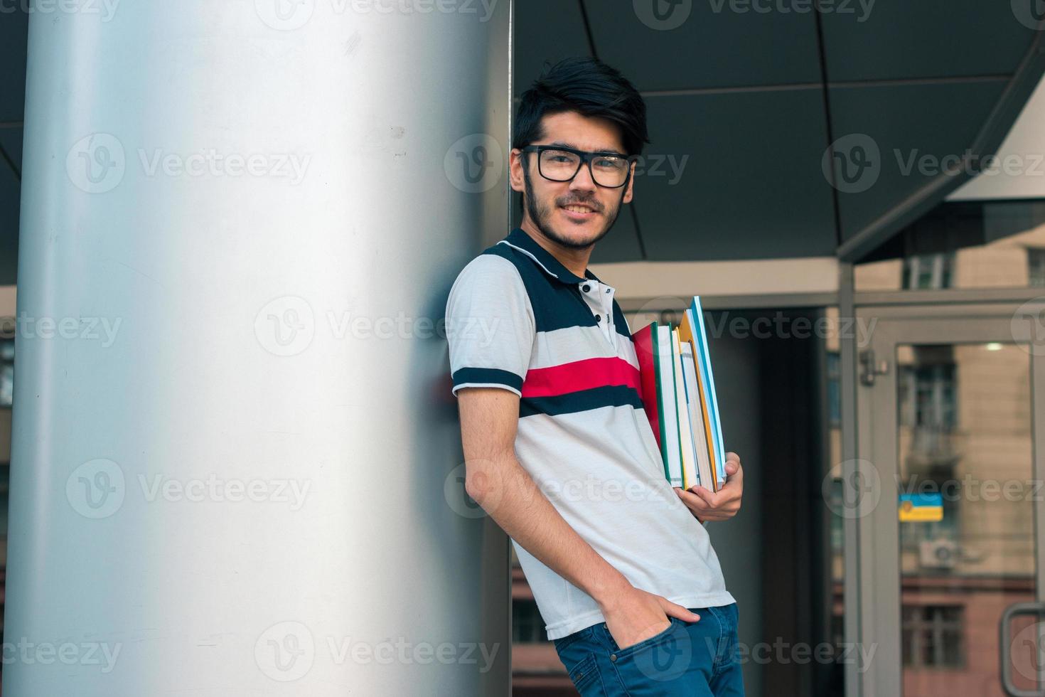 smiling nice guy stands near the columns keeps books photo