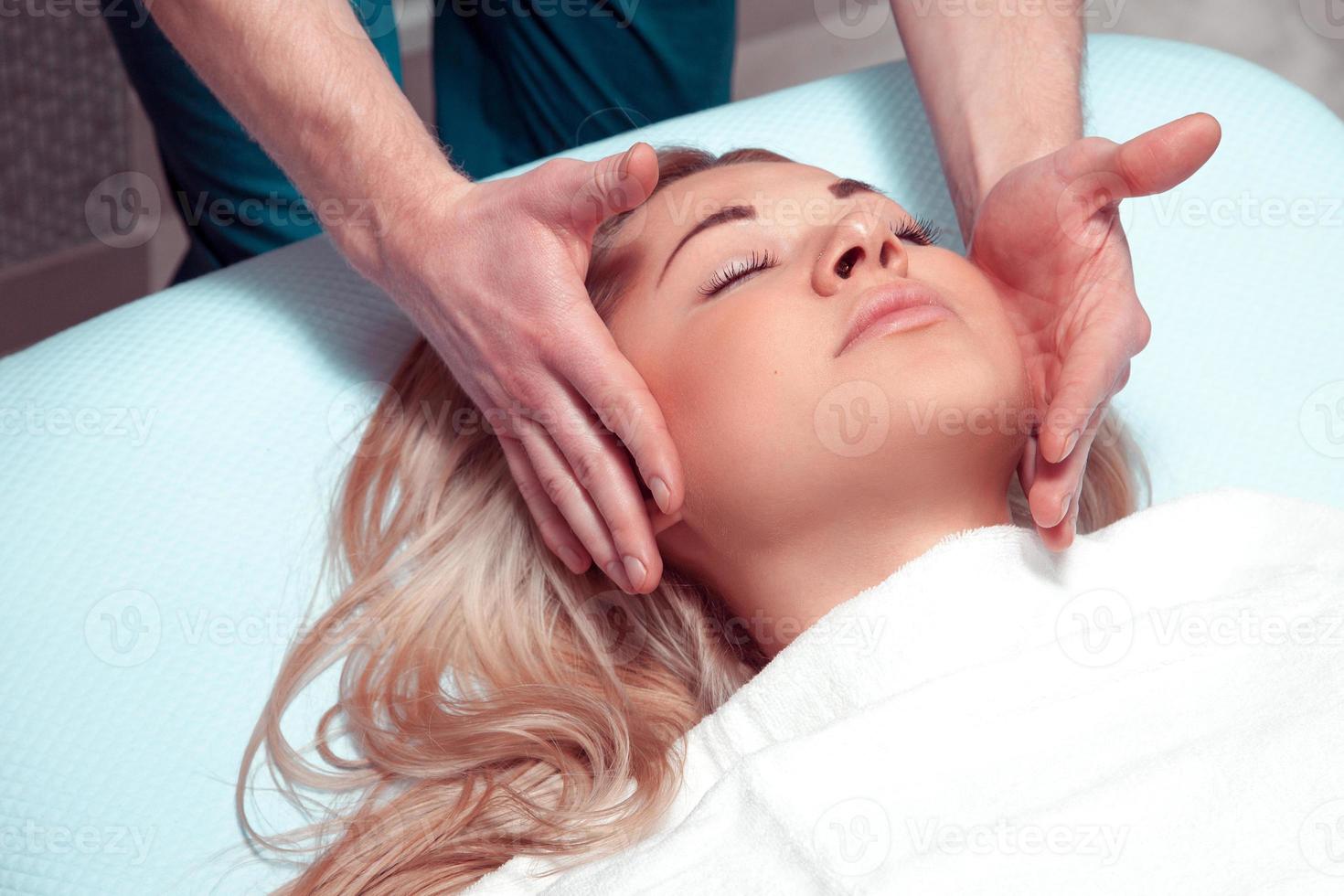 Masseur doing massage the head of an adult woman in the spa salon photo