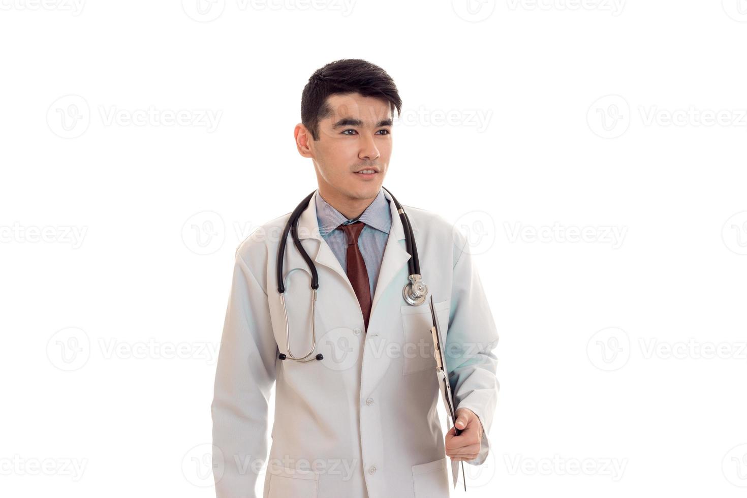 handsome young brunette man doctor in white uniform with stethoscope looking aside isolated in studio photo
