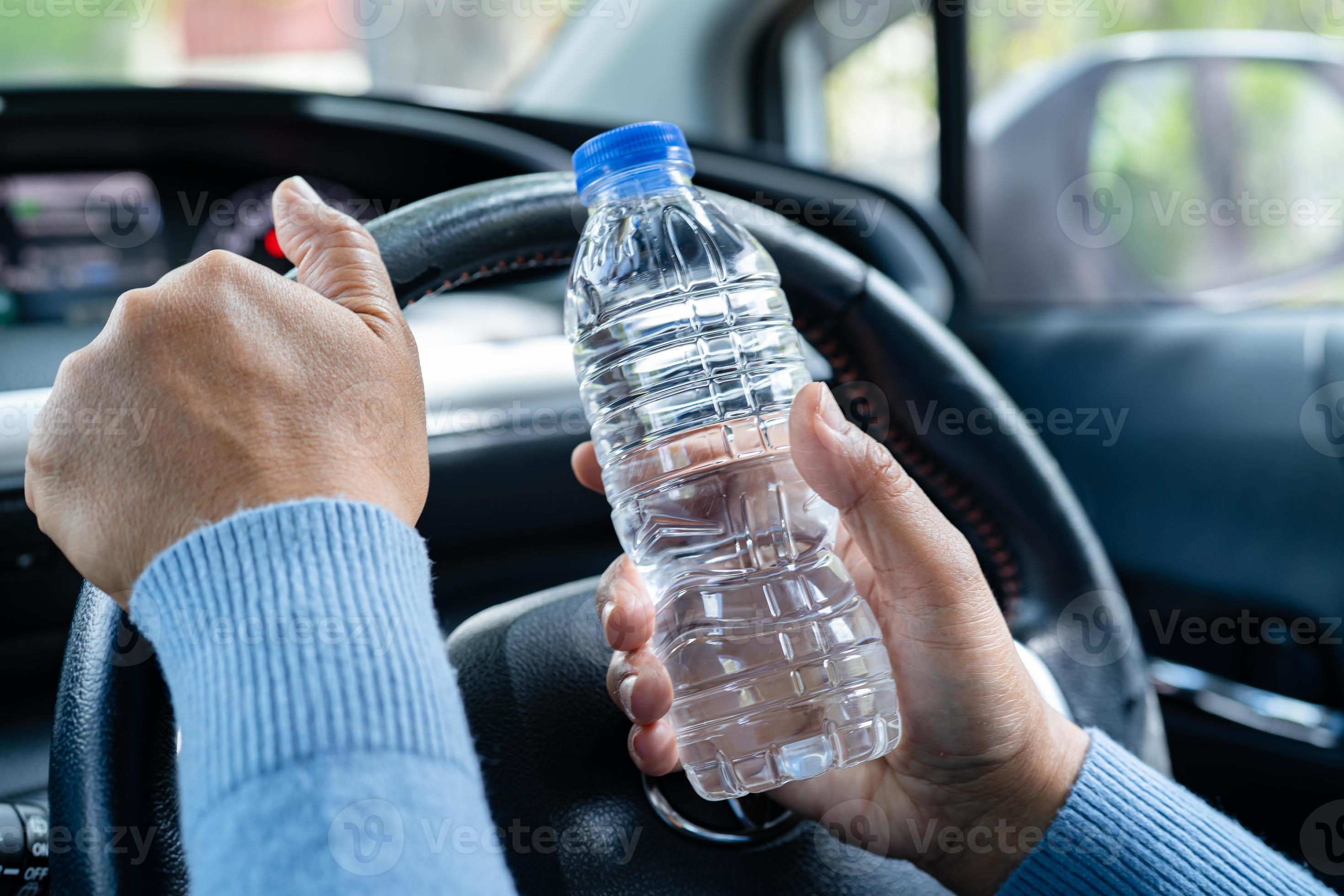 Asian woman driver holding bottle for drink water while driving a car. Plastic hot water bottle
