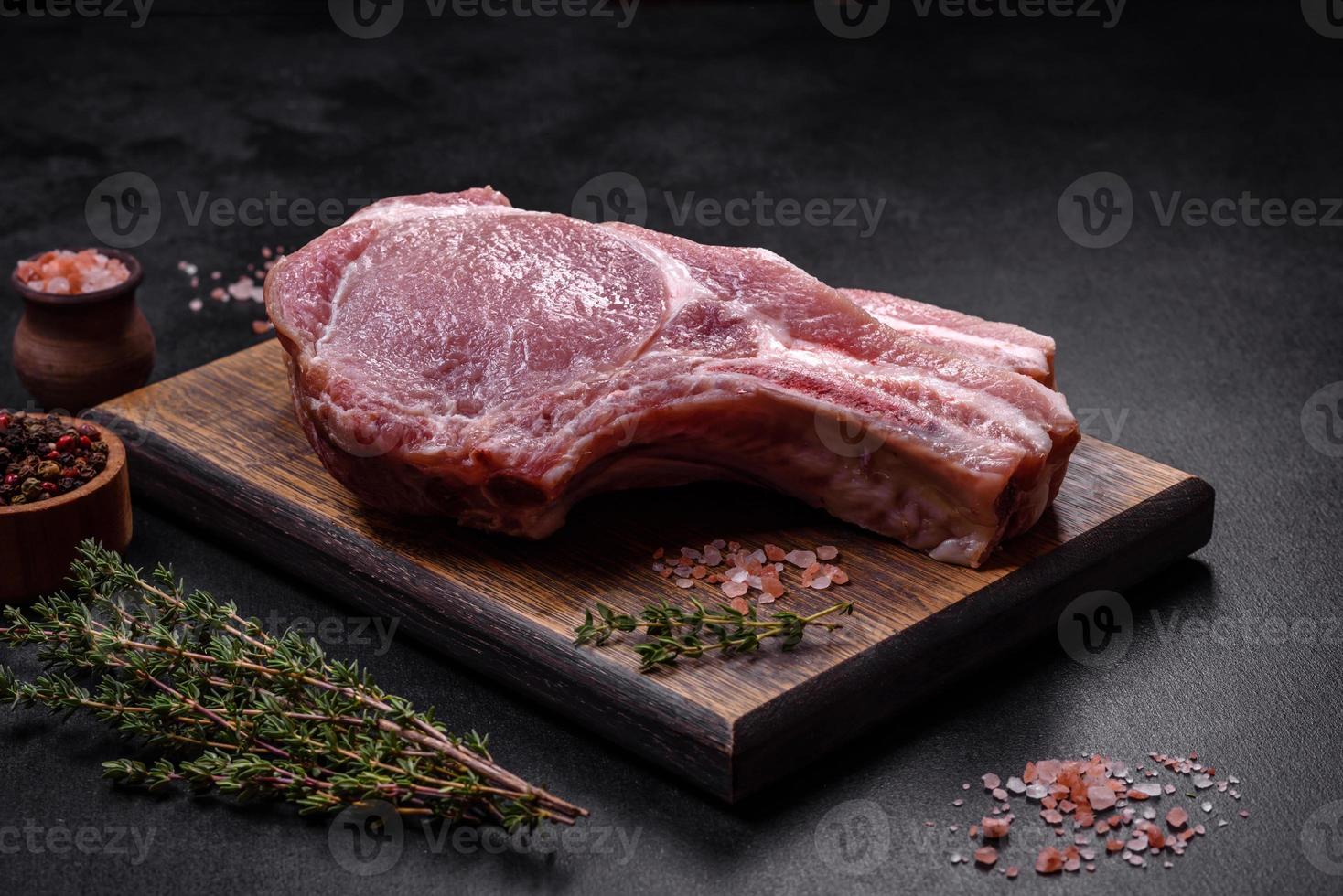 carne de cerdo cruda fresca en las costillas con especias y hierbas en una tabla de cortar de madera foto